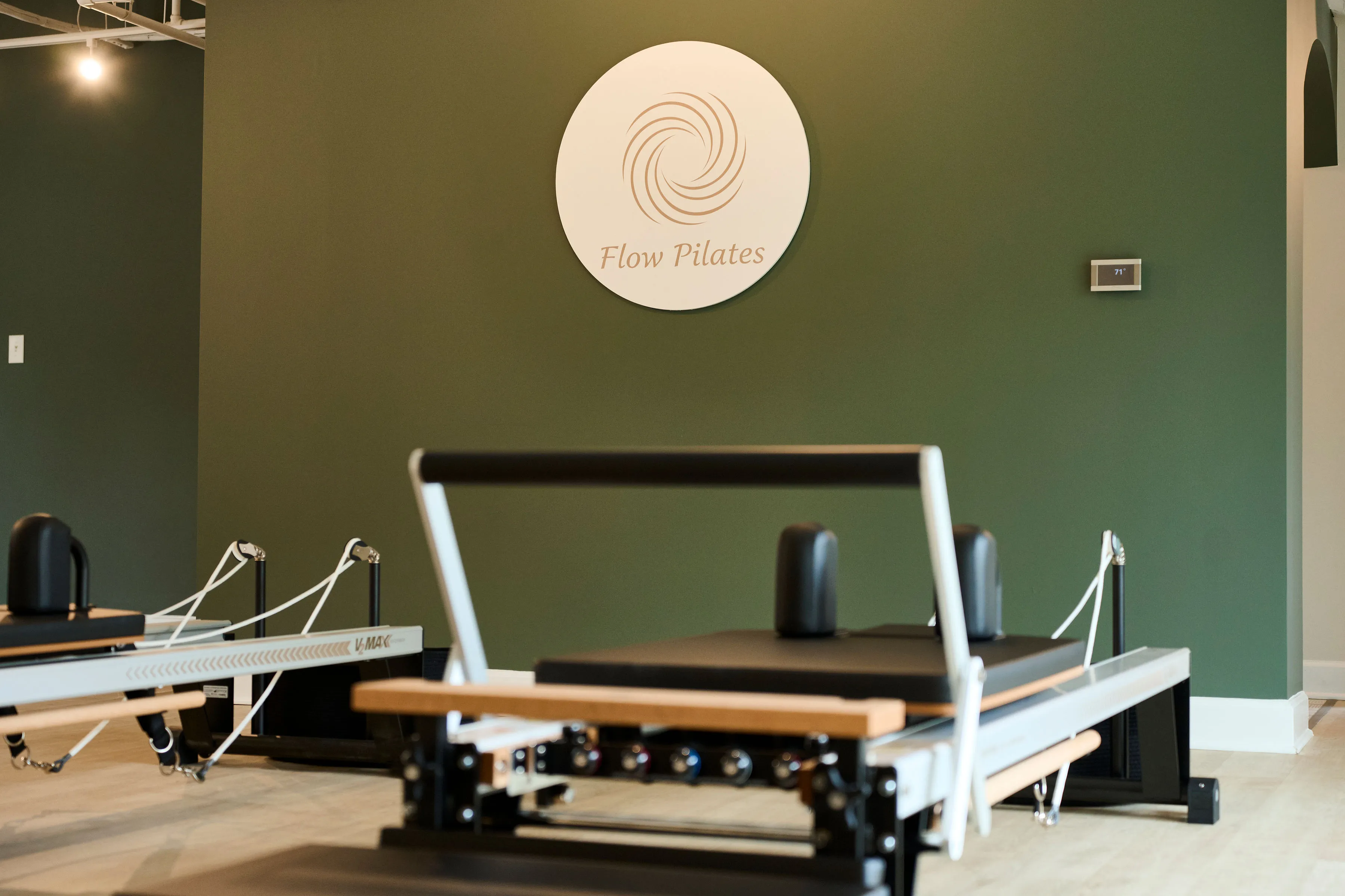 Flow Pilates logo on green wall with Merrithew reformer